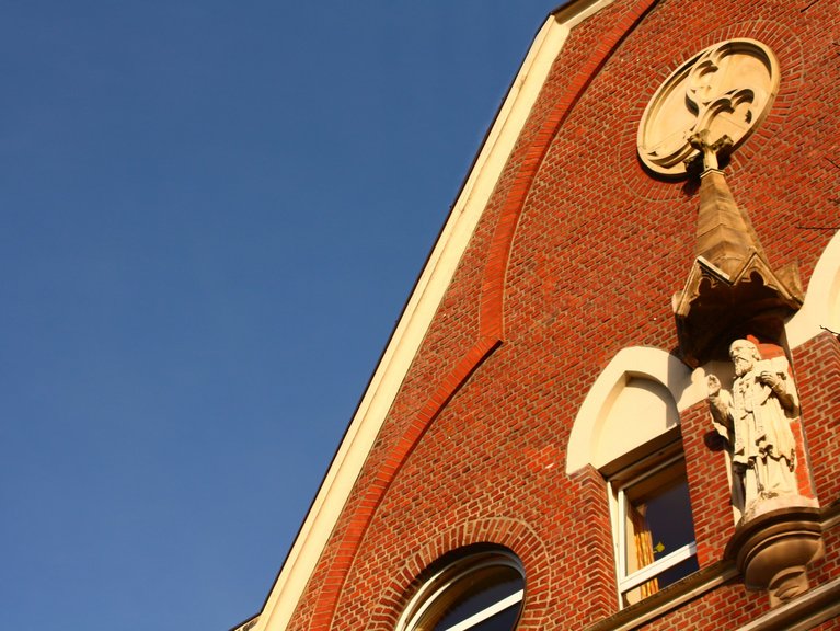 Hoch oben an der Fassade des Franz Sales Hauses sieht man eine Figur des Heiligen. 